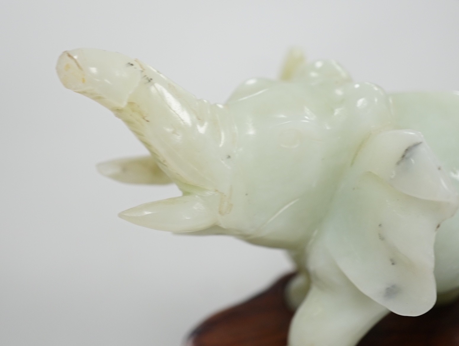 A Chinese bowenite jade elephant on hard wood stand, 11cm tall
